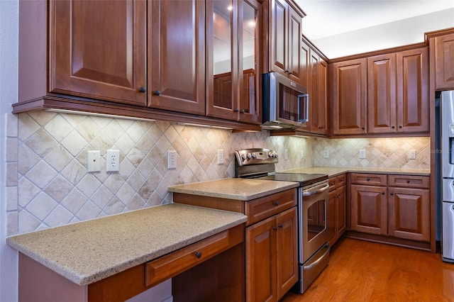 kitchen featuring decorative backsplash, light stone counters, light wood-type flooring, and stainless steel appliances