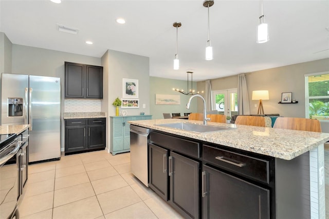 kitchen featuring sink, backsplash, decorative light fixtures, a center island with sink, and appliances with stainless steel finishes