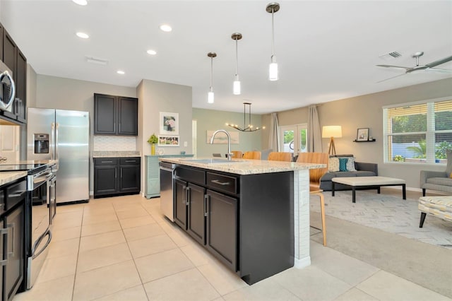 kitchen featuring appliances with stainless steel finishes, light stone counters, a breakfast bar, ceiling fan with notable chandelier, and a kitchen island with sink