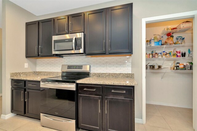 kitchen with appliances with stainless steel finishes, tasteful backsplash, light tile patterned floors, and light stone counters