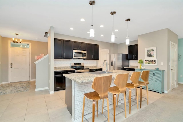 kitchen featuring sink, hanging light fixtures, stainless steel appliances, a kitchen bar, and a center island with sink