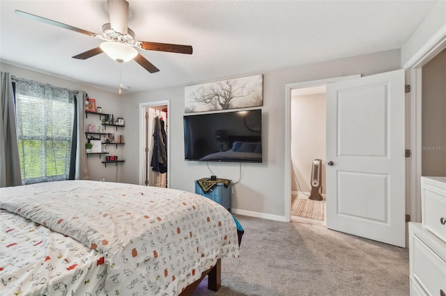 bedroom with a closet, baseboards, ceiling fan, a walk in closet, and light carpet