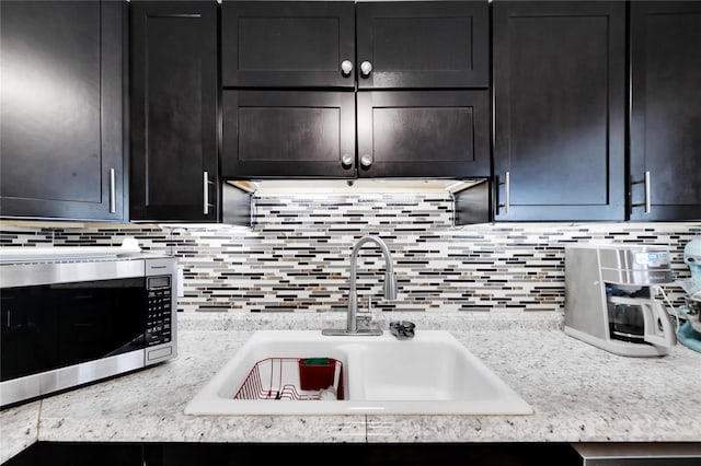 kitchen with tasteful backsplash, light stone countertops, and sink