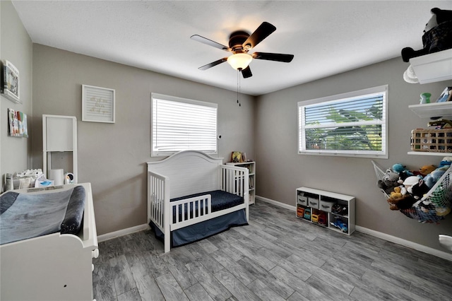 bedroom with wood-type flooring, a nursery area, and ceiling fan