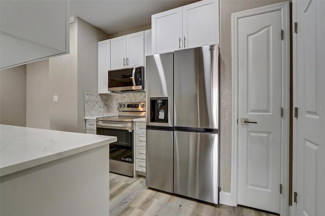 kitchen featuring decorative backsplash, light wood-type flooring, light stone counters, white cabinetry, and stainless steel appliances