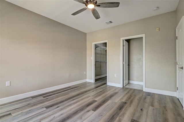 unfurnished bedroom with a walk in closet, light hardwood / wood-style flooring, a closet, and ceiling fan