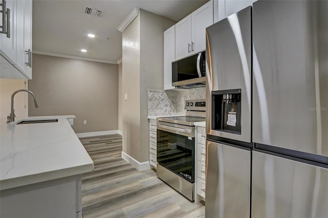 kitchen featuring light stone countertops, appliances with stainless steel finishes, sink, light hardwood / wood-style flooring, and white cabinetry