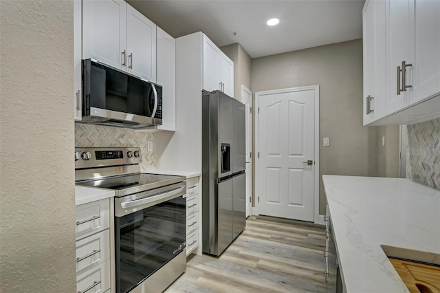 kitchen featuring white cabinetry, light wood-type flooring, light stone counters, and appliances with stainless steel finishes