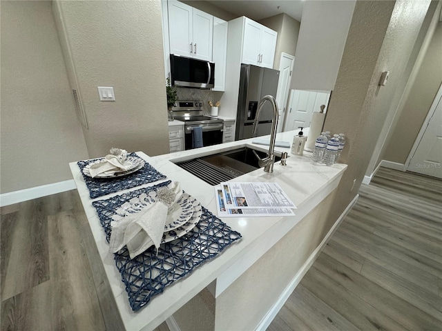 kitchen featuring baseboards, appliances with stainless steel finishes, white cabinets, and wood finished floors