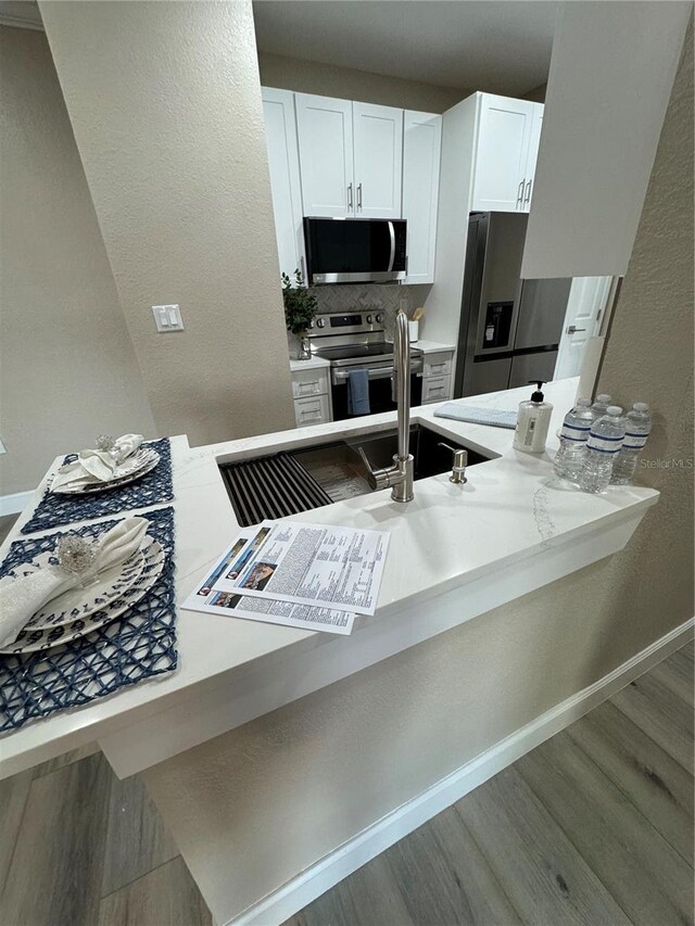 kitchen with wood finished floors, white cabinetry, baseboards, appliances with stainless steel finishes, and tasteful backsplash