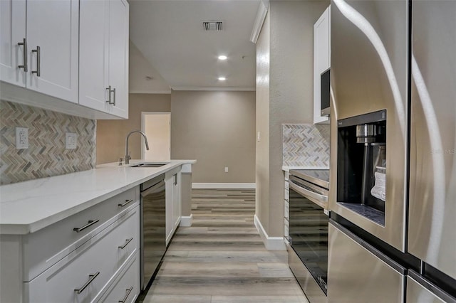 kitchen featuring stainless steel appliances, a sink, visible vents, ornamental molding, and light wood-type flooring