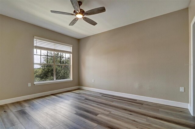 spare room with wood finished floors, a ceiling fan, and baseboards