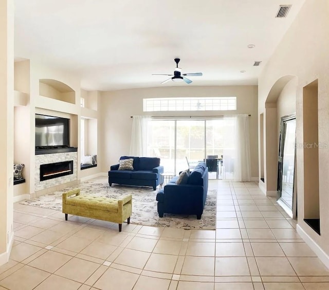 living room with light tile patterned floors, ceiling fan, and a stone fireplace