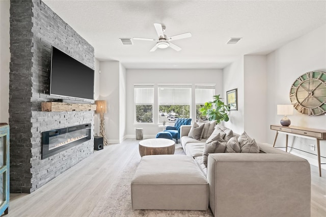 living room with ceiling fan, light wood-style floors, a fireplace, and visible vents