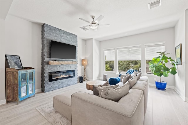 living room featuring visible vents, baseboards, wood finished floors, a ceiling fan, and a stone fireplace