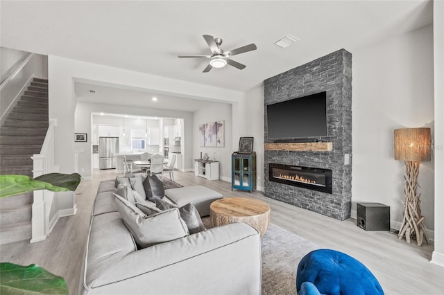 living area with stairway, wood finished floors, a stone fireplace, visible vents, and ceiling fan