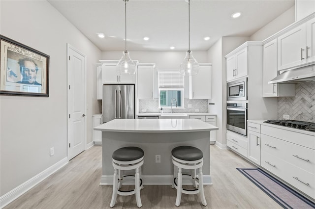 kitchen featuring light countertops, white cabinetry, a center island, under cabinet range hood, and stainless steel appliances