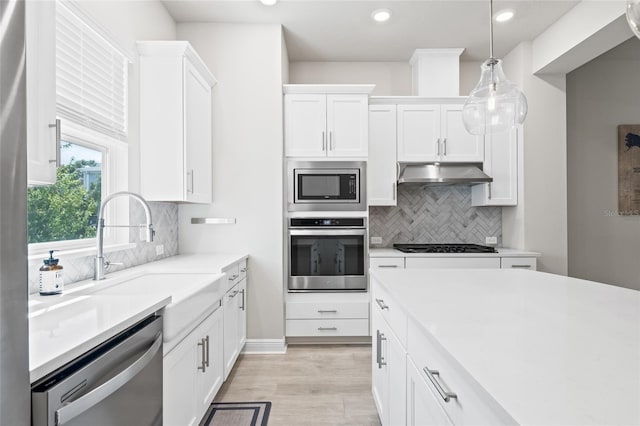 kitchen with light countertops, a sink, white cabinetry, appliances with stainless steel finishes, and under cabinet range hood