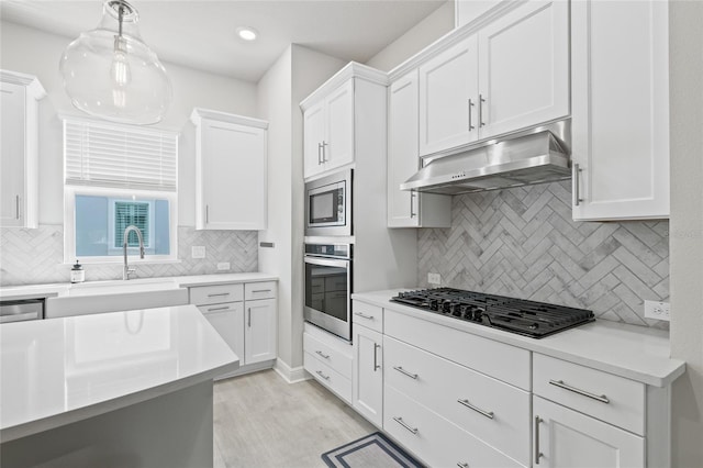kitchen with white cabinets, light countertops, appliances with stainless steel finishes, under cabinet range hood, and a sink