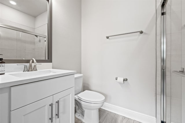 full bathroom with wood finished floors, toilet, tiled shower, and vanity