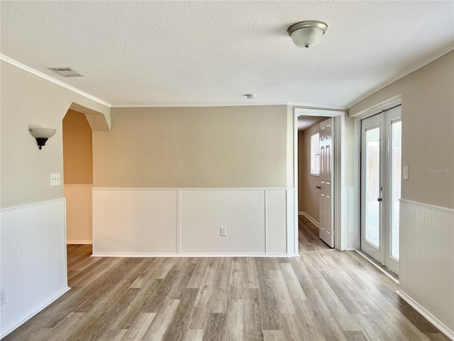 empty room featuring a textured ceiling, light hardwood / wood-style flooring, and crown molding