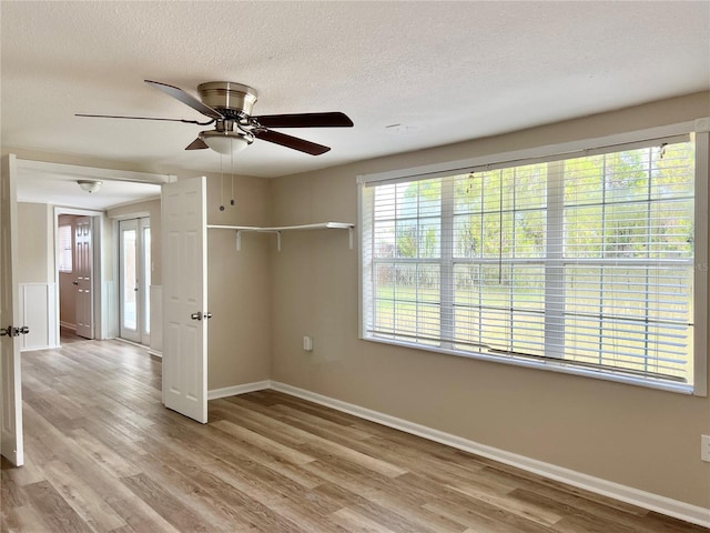 empty room with light wood-type flooring, ceiling fan, and a textured ceiling