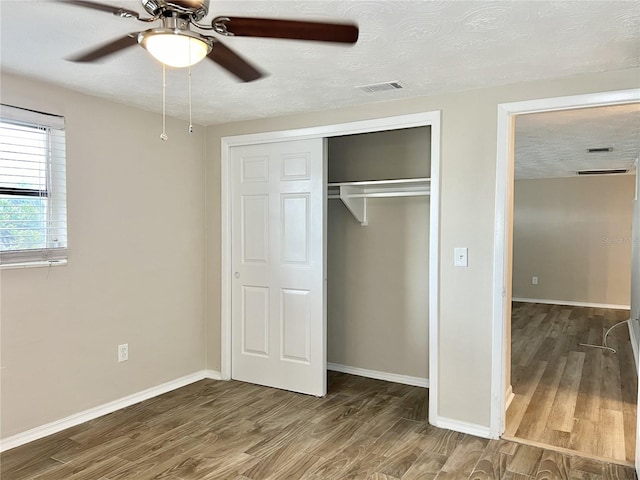 unfurnished bedroom with a textured ceiling, ceiling fan, a closet, and wood-type flooring