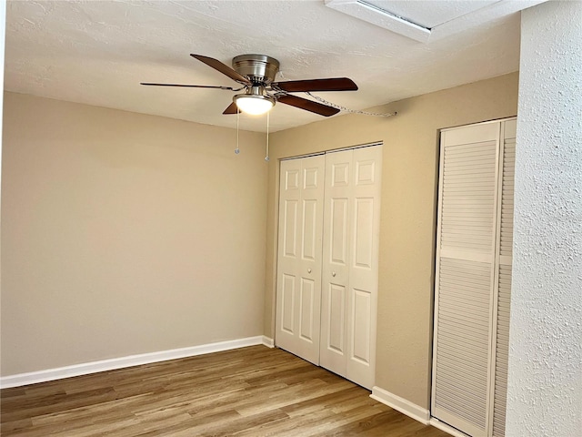 unfurnished bedroom featuring two closets, ceiling fan, hardwood / wood-style flooring, and a textured ceiling