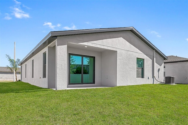 back of property with central AC unit, stucco siding, and a yard