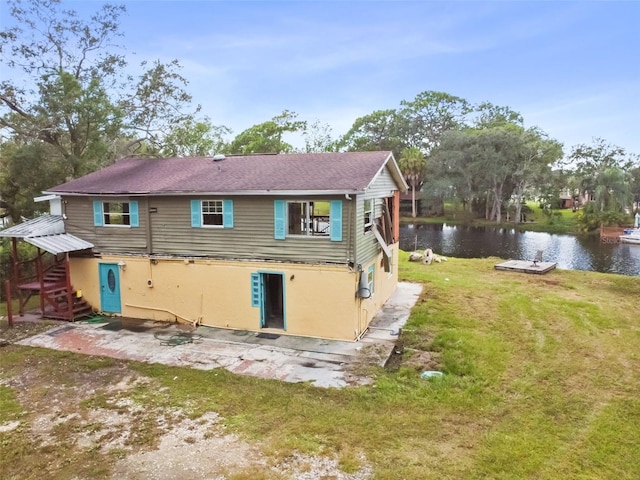 rear view of house featuring stucco siding, a water view, and a lawn