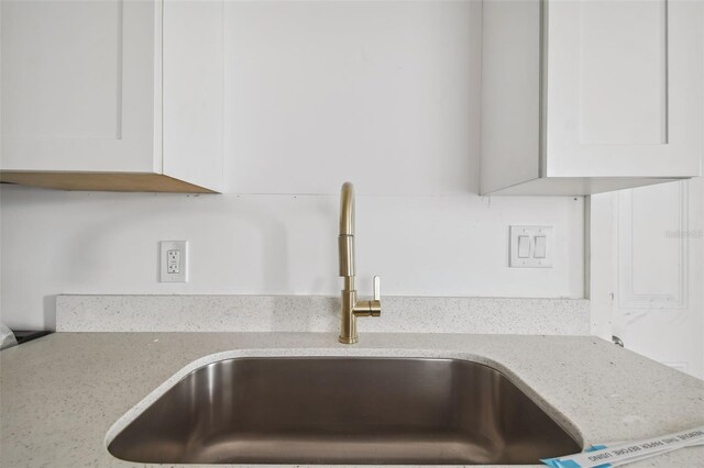 interior details featuring light stone counters, white cabinetry, and sink