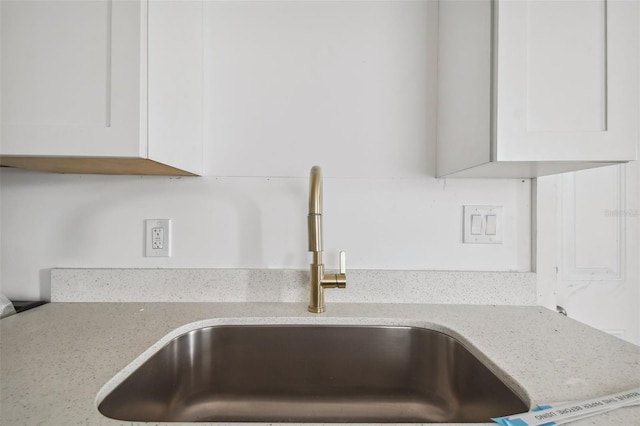 room details featuring white cabinets, light stone counters, and a sink