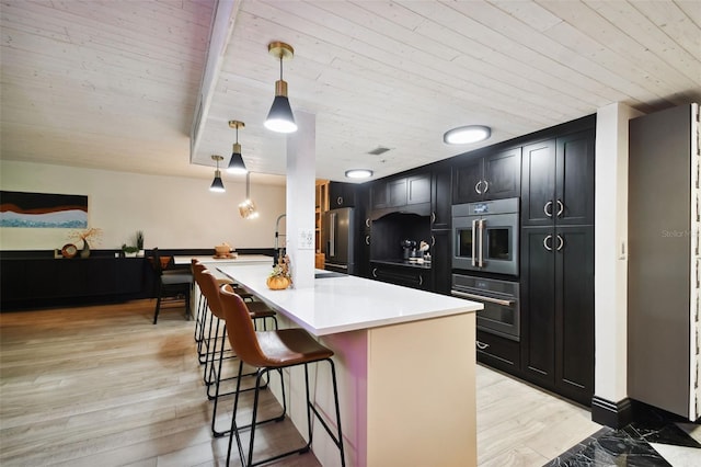 kitchen featuring hanging light fixtures, light hardwood / wood-style floors, stainless steel fridge, a kitchen breakfast bar, and a kitchen island with sink