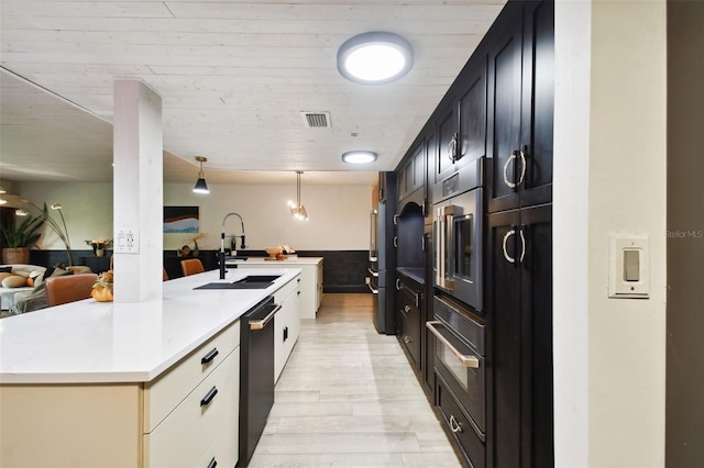 kitchen featuring light hardwood / wood-style floors, sink, black appliances, cream cabinetry, and a kitchen island with sink