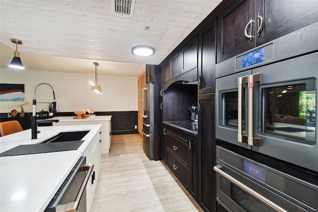 kitchen with appliances with stainless steel finishes, hanging light fixtures, light hardwood / wood-style floors, and sink