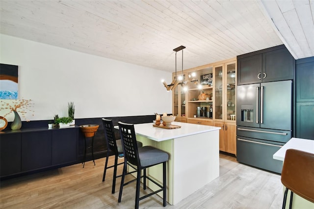 kitchen featuring decorative light fixtures, built in fridge, a center island, a breakfast bar area, and light hardwood / wood-style floors