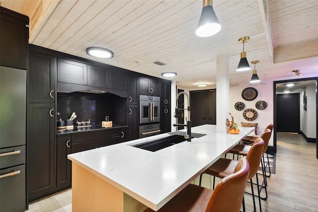 kitchen featuring a kitchen island with sink, a kitchen bar, hanging light fixtures, wood ceiling, and light hardwood / wood-style floors