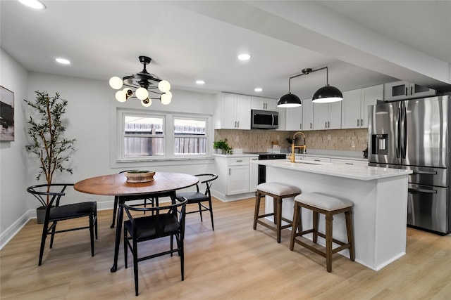 kitchen with a kitchen island with sink, appliances with stainless steel finishes, decorative light fixtures, and white cabinets