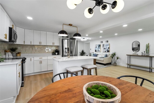 kitchen featuring pendant lighting, light hardwood / wood-style floors, a kitchen island with sink, stainless steel appliances, and white cabinets