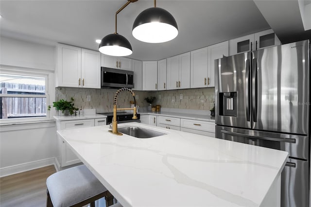 kitchen with appliances with stainless steel finishes, an island with sink, sink, decorative backsplash, and light stone counters