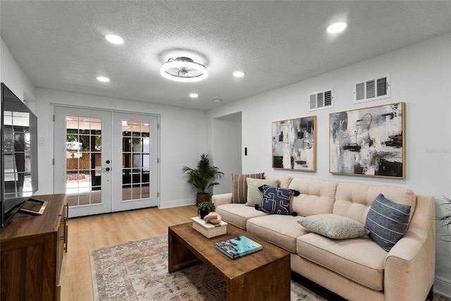 living room featuring a textured ceiling, light hardwood / wood-style flooring, and french doors