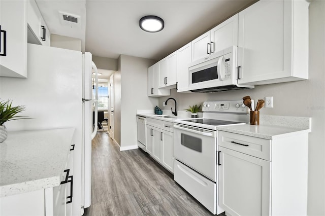 kitchen with light wood-type flooring, white cabinetry, white appliances, sink, and light stone countertops