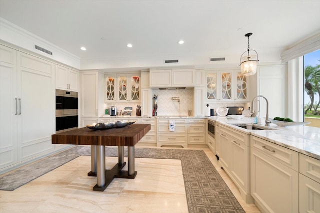 kitchen featuring light stone countertops, backsplash, crown molding, hanging light fixtures, and sink