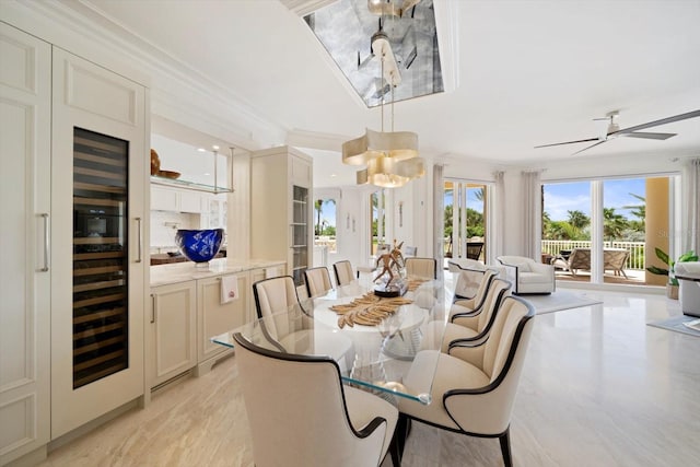 dining area featuring beverage cooler, ceiling fan with notable chandelier, and crown molding