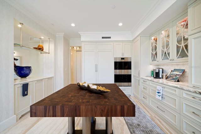 kitchen featuring light stone countertops, crown molding, white cabinetry, light wood-type flooring, and double oven