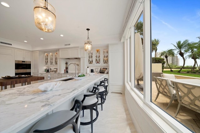 kitchen featuring hanging light fixtures, backsplash, sink, a kitchen bar, and ornamental molding