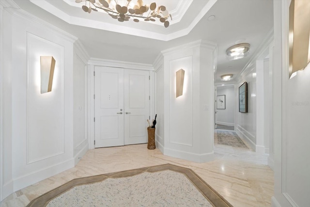 entryway with crown molding, a raised ceiling, and a chandelier