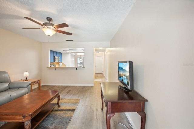 living room featuring a textured ceiling, ceiling fan, and light wood-type flooring