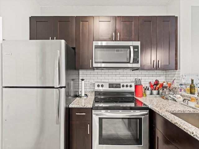 kitchen with light stone countertops, stainless steel appliances, dark brown cabinets, tasteful backsplash, and a textured ceiling