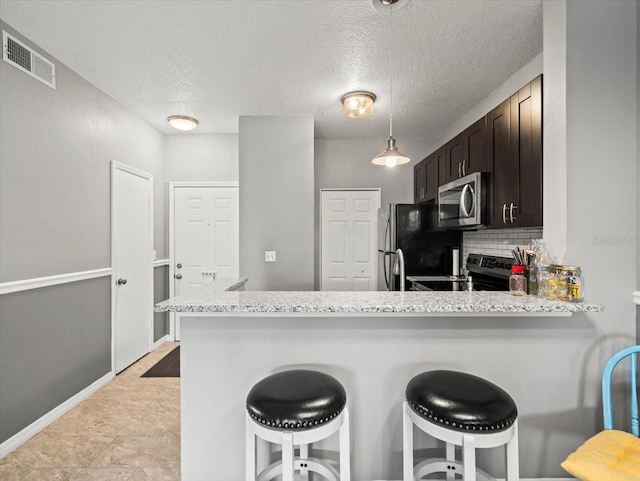 kitchen with stainless steel appliances, kitchen peninsula, decorative backsplash, a breakfast bar, and dark brown cabinetry